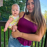 Sabrina is registered to the contest to win money with this photo: baby, blue_sky, casual_clothing, child, daylight, denim_skirt, flower_dress, greenery, happy, holding, nature, outdoor, person, porch, portrait, purple_top, smile, sunlight, trees, young_woman