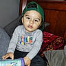 Juilo is registered to the contest to win money with this photo: toddler, child, cap, green_cap, sitting, bed, pillow, blanket, shirt, long_sleeve, cup, cartoon, indoor, curious, clothing, young_child, face, person, casual, home
