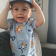 Juilo is registered to the contest to win money with this photo: toddler, child, hat, bluey, shirt, couch, living_room, smiling, happy, person, indoors, furniture, home, decor, wall_art, short_sleeves, gesture, casual_clothing, young_child, cute