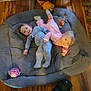 baby, babies, child, pajamas, gray_pet_bed, toy, wooden_floor, footwear, medical_boot, pink_clothing, blue_clothing, indoor, candid, playful, blurred_motion, toddler, soft_furniture, flooring, person, home