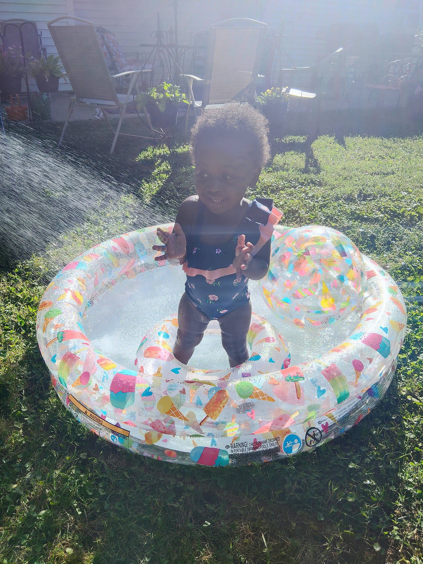 Estyr is registered to the contest to win money with this photo: backyard, chair, child, clapping, daytime, fun, garden, grass, happy, inflatable_pool, outdoor, plant, play, summer, sunlight, swimsuit, toddler, toy_ball, water, water_splash