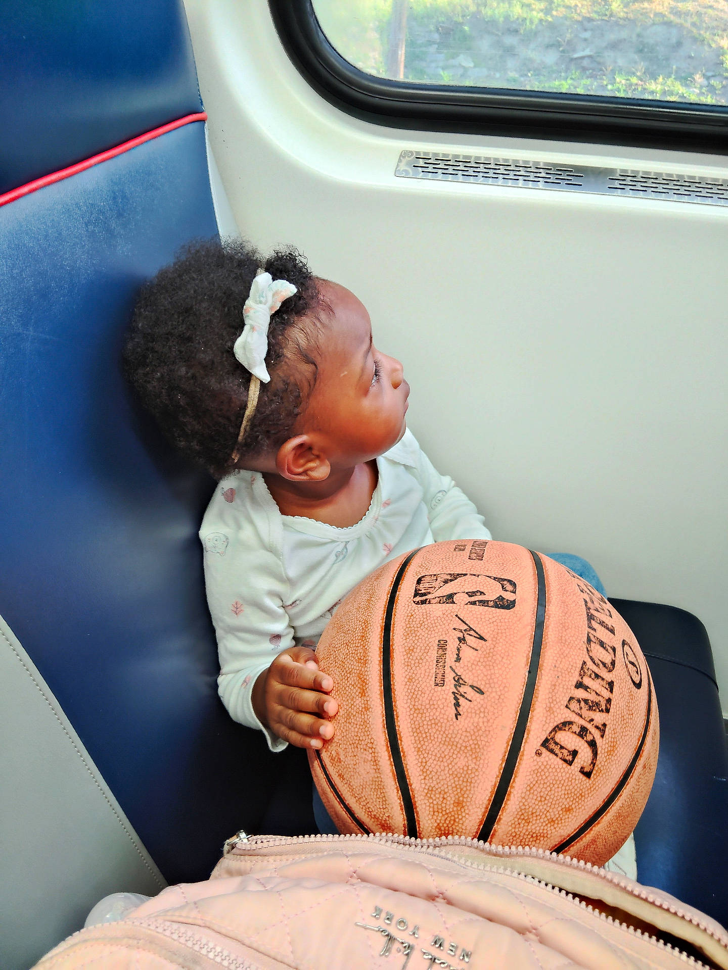 Estyr is registered to the contest to win money with this photo: bag, basketball, casual, child, clothing, curly_hair, cute, hand, headband, holding, indoor, looking, person, seat, side_view, toddler, transport, travel, window, young_child