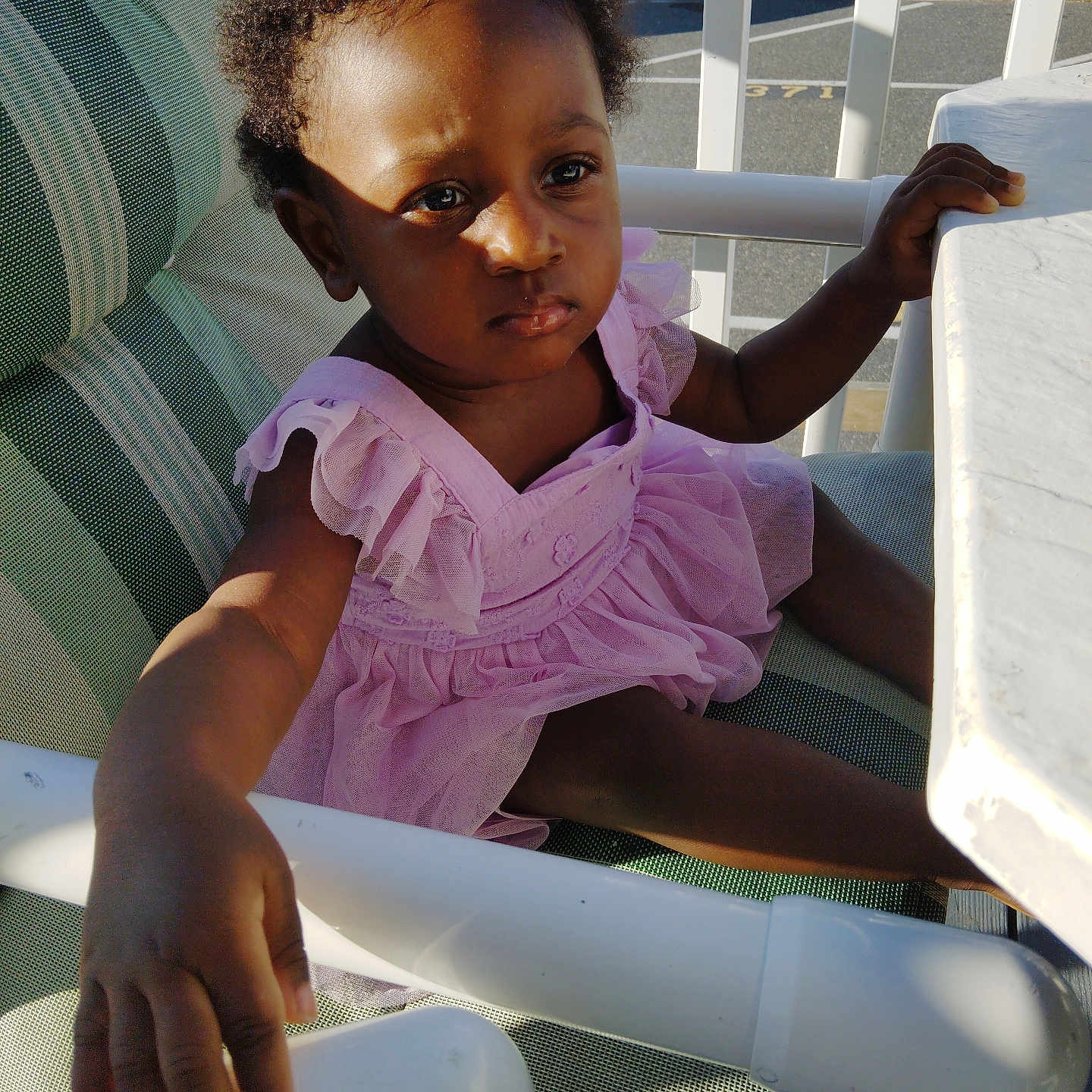 Estyr joined the competition — help win amazing prizes! balcony, chair, child, clothing, curly_hair, daylight, face, furniture, hand, outdoor, person, pink_dress, portrait, railing, serious_expression, sitting, skin, sunlight, table, toddler