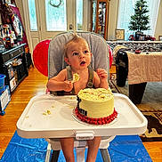 Charles is registered to the contest to win money with this photo: child, baby, high_chair, cake, birthday, frosting, messy, indoor, home, wood_floor, balloon, table, window, curtains, carpet, cabinet, picture_frame, christmas_tree, footrest, face