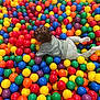 Talia a rejoint le concours — aidez-le/la à gagner de superbes lots ! back_of_head, ball_pit, bright_colors, brown_hair, child, colorful_balls, crawling, entertainment, family_activity, fun, indoor_playground, leisure, messy_play, pajamas, plastic_balls, play_area, playtime, socks, toddler, toys