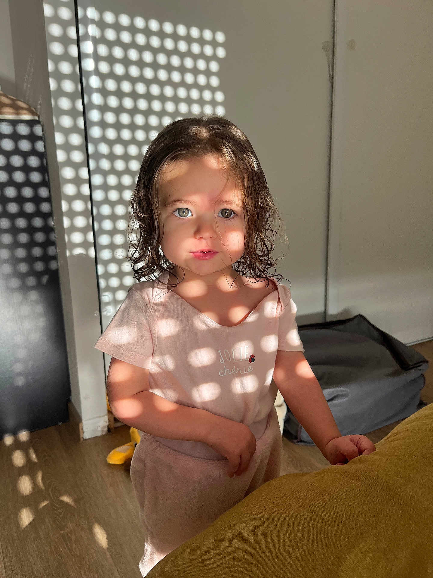 Talia a rejoint le concours — aidez-le/la à gagner de superbes lots ! toddler, child, indoor, sunlight, shadow_pattern, curly_hair, pink_clothing, face, portrait, wooden_floor, soft_light, cute, person, standing, expression, home_interior, wall, floor, playful_light, casual_clothing