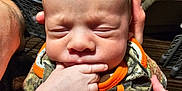 Alexander joined the competition — help win amazing prizes! baby, infant, hand, fingers, clothing, camouflage, orange, person, indoor, newborn, face, expression, cute, skin, sleeping, closeup, holding, adult_hand, portrait, child