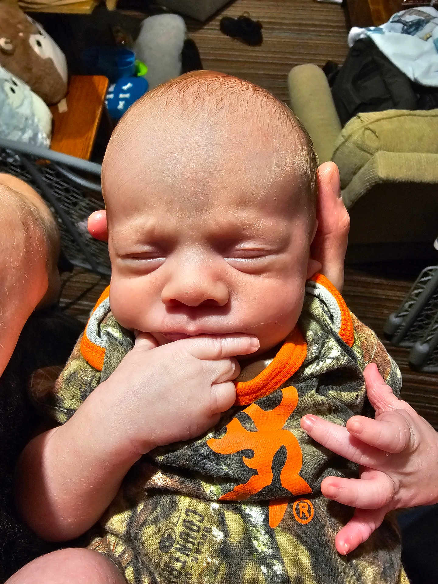 Alexander joined the competition — help win amazing prizes! baby, infant, hand, fingers, clothing, camouflage, orange, person, indoor, newborn, face, expression, cute, skin, sleeping, closeup, holding, adult_hand, portrait, child