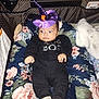baby, child, infant, costume, hat, purple, orange, floral, cushion, playpen, black_clothing, surprised, wide_eyes, indoors, blanket, fabric, person, cute, lying_down, holiday