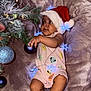 Thaïs participe au concours pour gagner de l'argent avec cette photo : baby, child, santa_hat, christmas_tree, ornament, holiday, lights, blanket, cute, infant, festive, decoration, indoor, smiling, celebration, christmas, person, portrait, reaching, soft