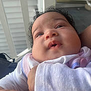 Evelyna is registered to the contest to win money with this photo: baby, child, closeup, clothing, curly_hair, cute, expression, face, hand, holding, infant, looking_up, outdoor, person, porch, railing, skin, soft, warm, young