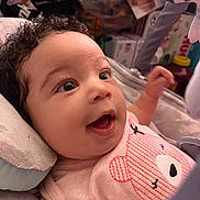 Evelyna joined the competition — help win amazing prizes! baby, infant, smiling, curly_hair, pink_clothing, bear_design, cushion, toy, indoor, closeup, happy, person, child, cute, expression, head, face, soft_toys, comfort, lying_down