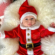 Adam is registered to the contest to win money with this photo: baby, child, santa_hat, christmas_costume, red_clothing, white_fur_trim, blue_eyes, fluffy_cushion, holiday, festive, portrait, cute, infant, soft_texture, holiday_season, smiling, indoors, warm, cozy, christmas