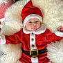 baby, child, santa_hat, christmas_costume, red_clothing, white_fur_trim, blue_eyes, fluffy_cushion, holiday, festive, portrait, cute, infant, soft_texture, holiday_season, smiling, indoors, warm, cozy, christmas