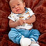 baby, blue_pants, child, construction_vehicle_print, cozy, cute, expression, face, happy, indoor, infant, onesie, plush_blanket, portrait, red_brown_background, sitting, small_hands, smiling, soft_texture, white_shoes