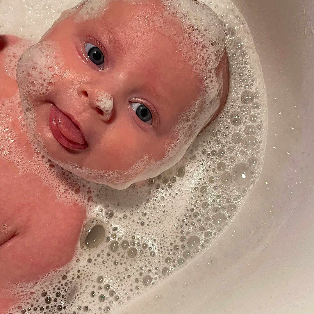 Eve is registered to the contest to win money with this photo: baby, bathing, bathtub, bubble, face, foam, head, newborn, person, photography, portrait, tub, washing