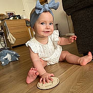 Ada a rejoint le concours — aidez-le/la à gagner de superbes lots ! baby, child, headband, bow, smile, floor, wooden_floor, milestone_plaque, indoor, furniture, dresser, toy, couch, hand, foot, person, clothing, happy, sitting, portrait