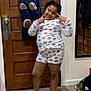 child, smiling, pajamas, peace_sign, indoor, door, wood, floor, socks, mirror, bag, shoes, happy, pose, person, clothing, hair, room, casual, fun