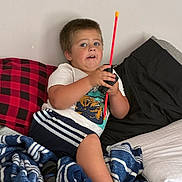 Steven is registered to the contest to win money with this photo: child, boy, bed, blanket, pillow, toy, walkie_talkie, clothing, shorts, tshirt, indoor, casual, expression, blue_eyes, hair, skin, home, comfort, relaxed, playful