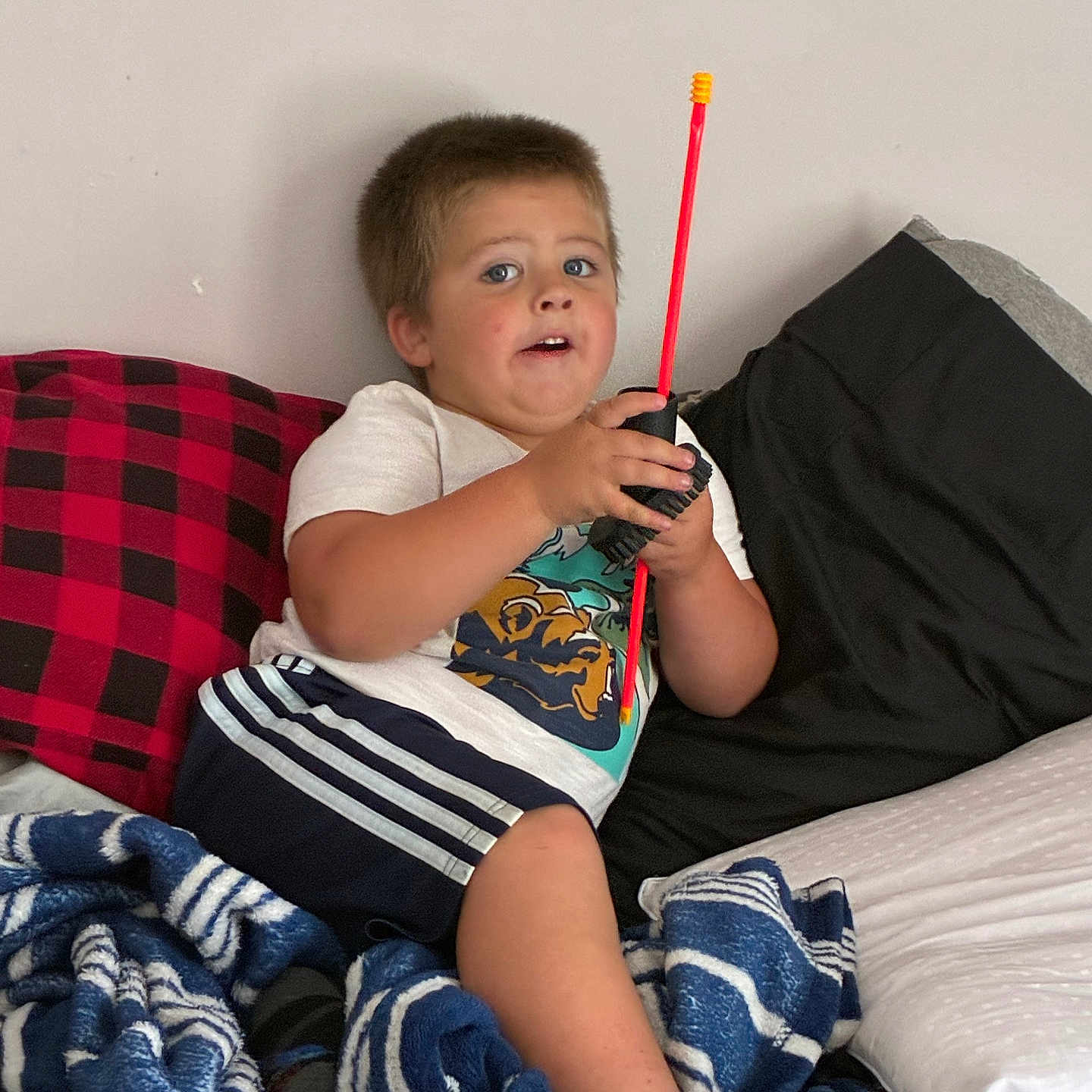 Steven is registered to the contest to win money with this photo: child, boy, bed, blanket, pillow, toy, walkie_talkie, clothing, shorts, tshirt, indoor, casual, expression, blue_eyes, hair, skin, home, comfort, relaxed, playful