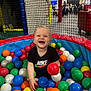 toddler, ball_pit, colorful_balls, black_tshirt, nike_logo, smiling_child, indoor_play_area, netting, playground, child, happy, toy, plastic_balls, fun, young_child, person, recreation, leisure, play, cute