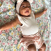 Yolanni joined the competition — help win amazing prizes! baby, child, infant, portrait, smiling, lying_down, floral_blanket, headband, bow, pink_outfit, romper, ruffles, bare_arms, legs, nursery, indoors, cozy, happy, closeup, photography