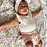 baby, bare_arms, bow, child, closeup, cozy, floral_blanket, happy, headband, indoors, infant, legs, lying_down, nursery, photography, pink_outfit, portrait, romper, ruffles, smiling