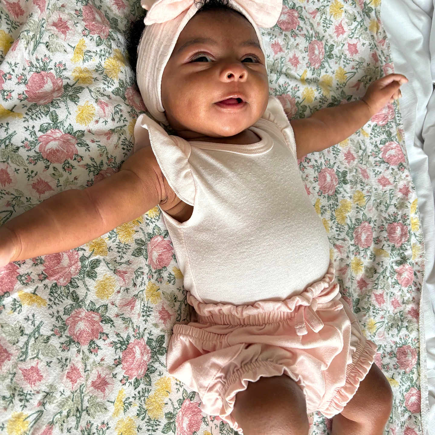 Yolanni joined the competition — help win amazing prizes! baby, child, infant, portrait, smiling, lying_down, floral_blanket, headband, bow, pink_outfit, romper, ruffles, bare_arms, legs, nursery, indoors, cozy, happy, closeup, photography