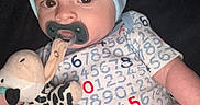 Lincoln joined the competition — help win amazing prizes! baby, black_background, blue_hat, child, close_up, clothing, face, head, indoors, infant, lying_down, number_pattern, onesie, pacifier, plush_toy, portrait, sitting, stuffed_cow, toy, wide_eyes