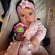 Fernanda is registered to the contest to win money with this photo: baby, child, car_seat, pink_headband, flower, toy, blanket, onesie, bear_pattern, curious_eyes, hand, clothing, infant, cute, indoor, seatbelt, portrait, soft_toy, baby_accessory, cozy