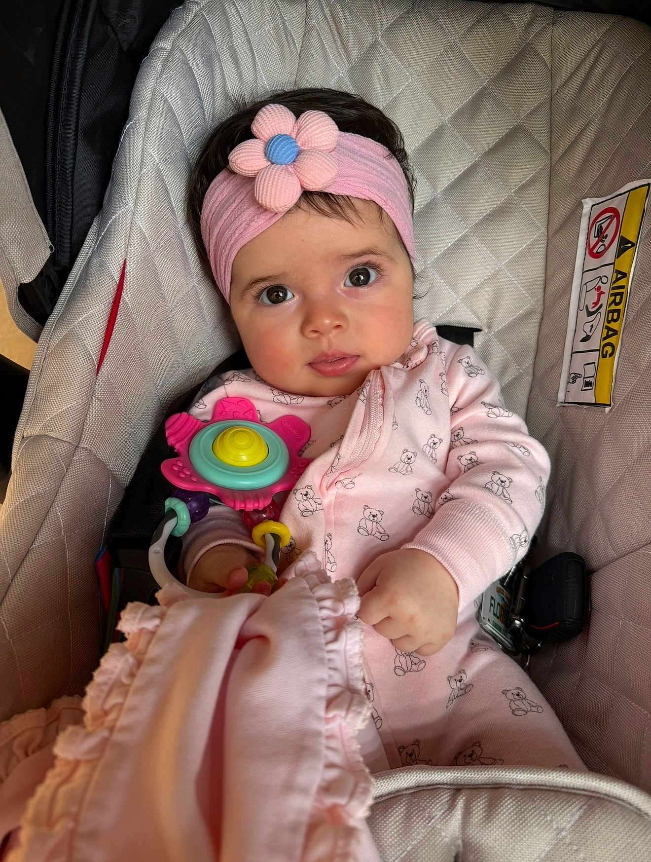 Fernanda is registered to the contest to win money with this photo: baby, child, car_seat, pink_headband, flower, toy, blanket, onesie, bear_pattern, curious_eyes, hand, clothing, infant, cute, indoor, seatbelt, portrait, soft_toy, baby_accessory, cozy