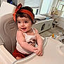 baby, child, high_chair, headband, indoor, smile, happy, curly_hair, clothing, infant, person, furniture, window_blinds, toy, cat_tree, modern_interior, cute, playful, portrait, skin