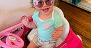 Raelynn is registered to the contest to win money with this photo: accessories, baby, bodypart, clothing, face, finger, glasses, hand, head, hosiery, machine, person, photography, portrait, shorts, sitting, sock, sunglasses, t_shirt, wheel