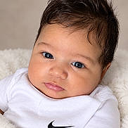 Laosval is registered to the contest to win money with this photo: baby, child, infant, portrait, close_up, face, eyes, brown_hair, white_shirt, nike, logo, lying_down, blanket, fluffy_blanket, indoor, soft_lighting, adorable, serious_expression, headshot, photography