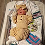 Tilly-Mae is registered to the contest to win money with this photo: newborn, baby, sleeping, infant, bassinet, hospital, blanket, clothing, headband, bow, mittens, socks, ornament, name_tag, wood_floor, cozy, resting, cute, portrait, indoor