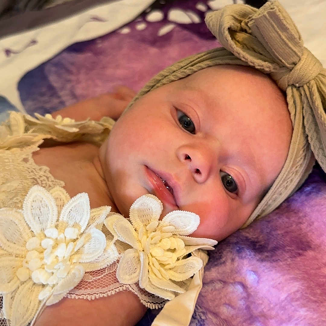 Ella is registered to the contest to win money with this photo: adult, baby, bodypart, bonnet, clothing, face, finger, glove, hand, hat, head, homedecor, linen, male, man, newborn, person, photography, portrait, purple