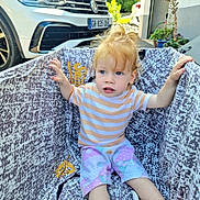 Lùcia participe au concours pour gagner de l'argent avec cette photo : blue_eyes, car, casual, child, curious, curly_hair, greenery, grip, hand, outdoor, patterned_fabric, playpen, shorts, sitting, striped_shirt, suburban, sunlight, toddler, vehicle, young_child