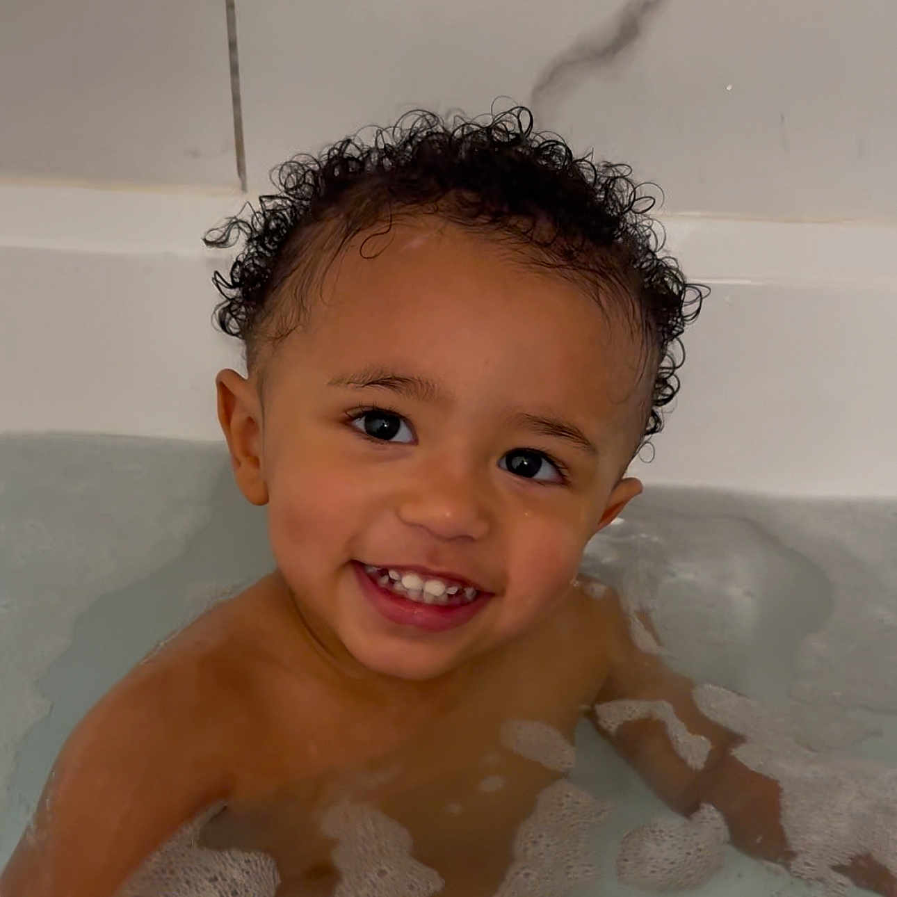 Kavani is registered to the contest to win money with this photo: baby, back, bathing, bathtub, bodypart, face, finger, hand, happy, head, mouth, person, photography, portrait, smile, tub
