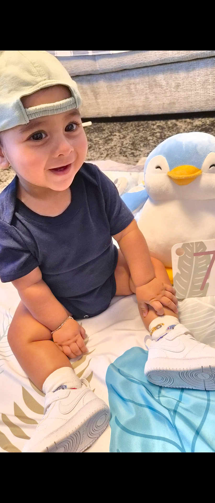 Zaaviar participe au concours pour gagner de l'argent avec cette photo : toddler, child, baby, cap, sneakers, plush_toy, penguin, blanket, smiling, happy, indoor, cute, playing, footwear, sock, bracelet, card, number, sitting, person
