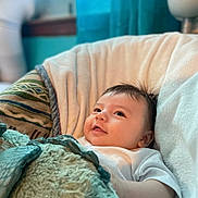 Micah is registered to the contest to win money with this photo: baby, blanket, chair, cozy, comfort, cute, face, infant, indoors, looking_up, portrait, resting, soft, smile, toddler, white_clothing, window, curtain, home, peaceful