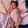 baby, infant, child, blanket, pink_bow, romper, sandals, curly_hair, lying_down, indoors, soft_texture, cute, portrait, person, skin, hand, footwear, face, expression, cozy