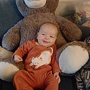 Océane participe au concours pour gagner de l'argent avec cette photo : baby, child, couch, cozy, cute, furniture, happy, home, indoor, infant, onesie, orange_clothing, person, playful, plush_toy, relaxing, seated, smiling, soft_toy, teddy_bear