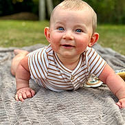 Gabriel participe au concours pour gagner de l'argent avec cette photo : baby, child, blue_eyes, smile, blanket, striped_shirt, outdoor, grass, face, skin, cheeks, hands, lying_down, curious, infant, portrait, cute, young, daylight, soft_texture