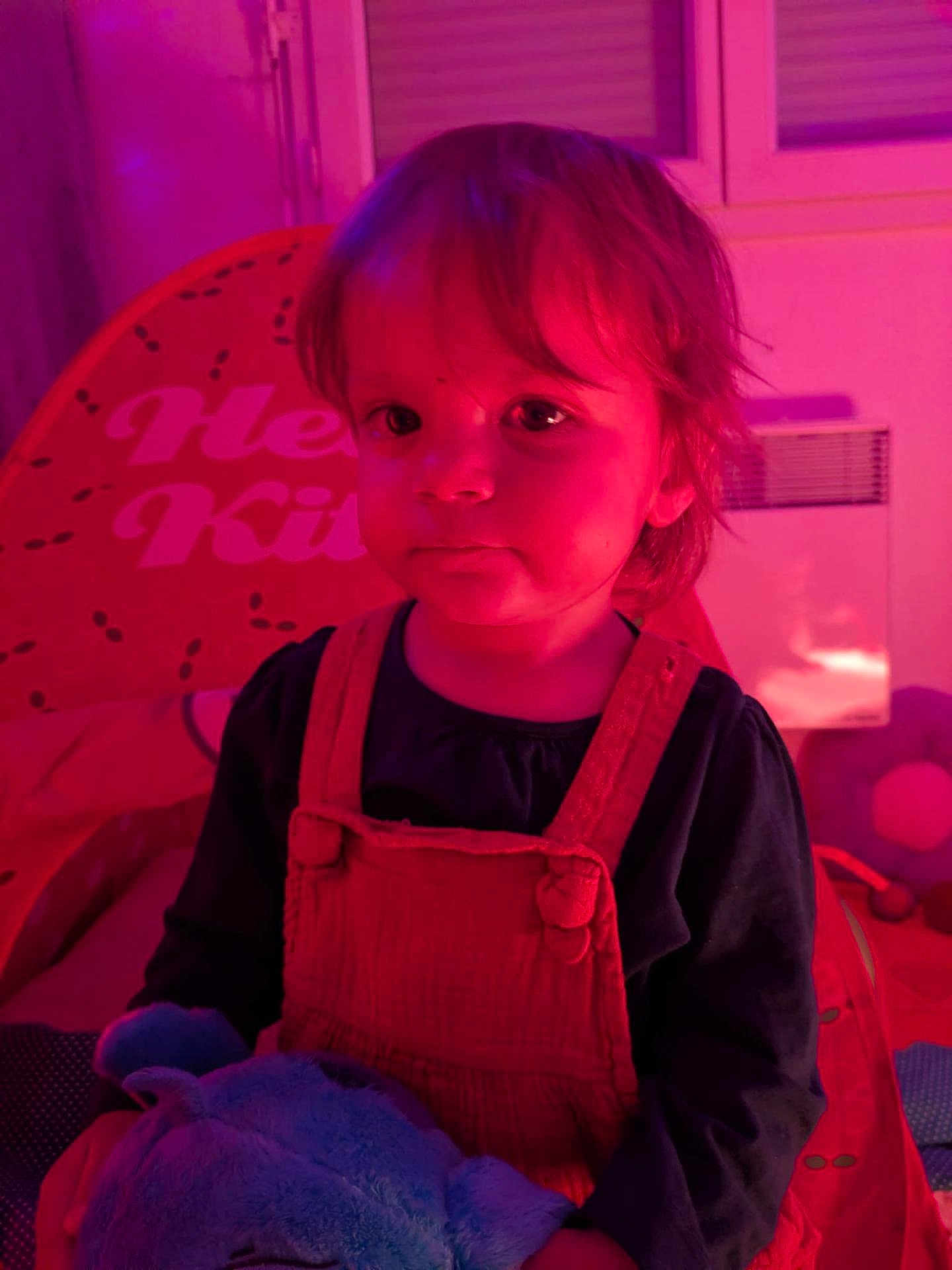 Elina participe au concours pour gagner de l'argent avec cette photo : toddler, child, plush_toy, pink_lighting, purple_lighting, hello_kitty, cushion, indoor, portrait, clothing, overalls, face, person, seated, toy, room, window, heater, casual, expression