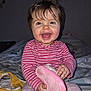 baby, child, smiling, happy, indoor, bed, clothing, pink_shoe, toddler, person, portrait, cute, hair, face, hand, sitting, striped_shirt, blanket, toy, home