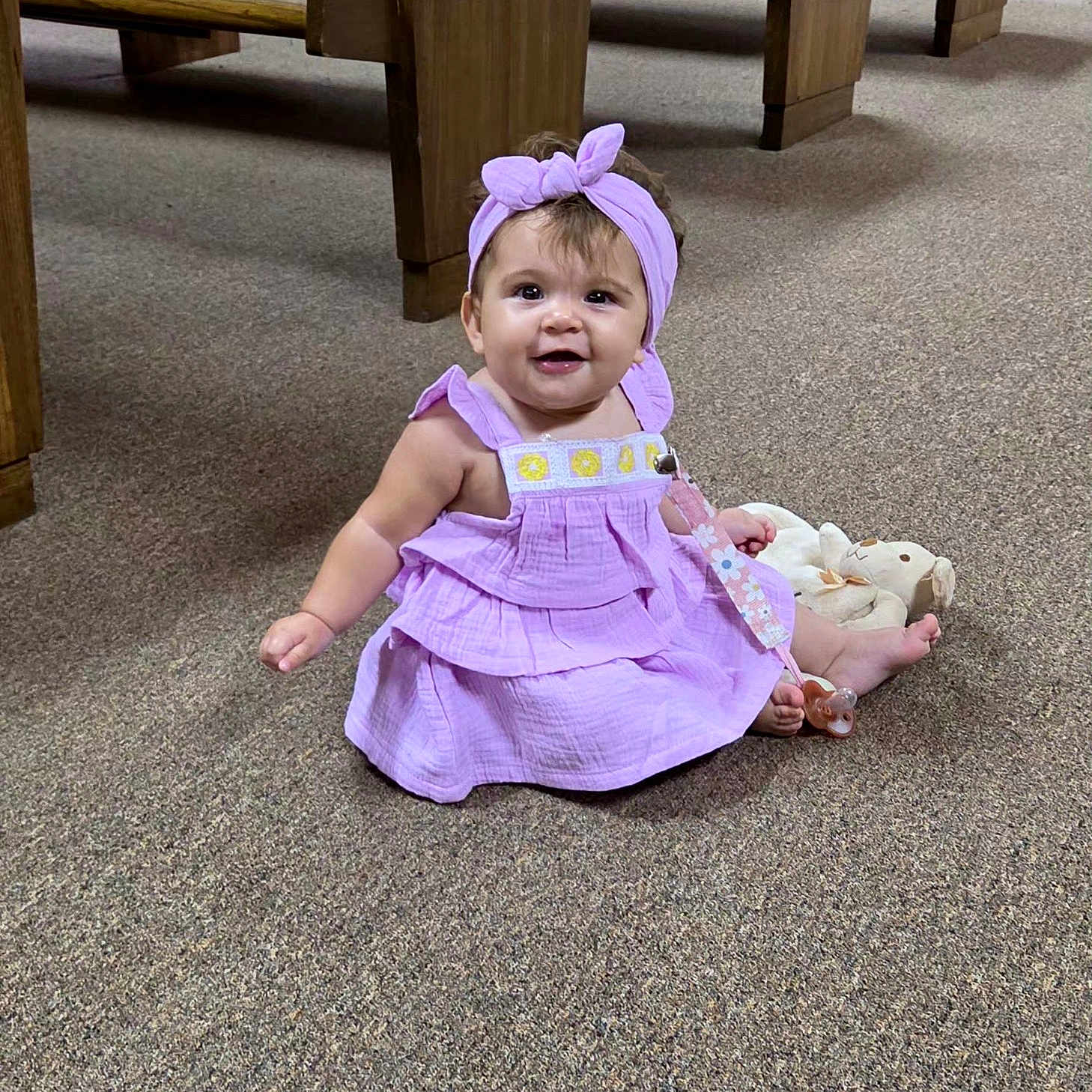 Maelee joined the competition — help win amazing prizes! baby, bow, carpet, child, church, floor, happy, headband, indoor, infant, lavender_dress, pacifier, photography, portrait, purple_clothing, sitting, smiling, stuffed_animal, toy, wooden_pews