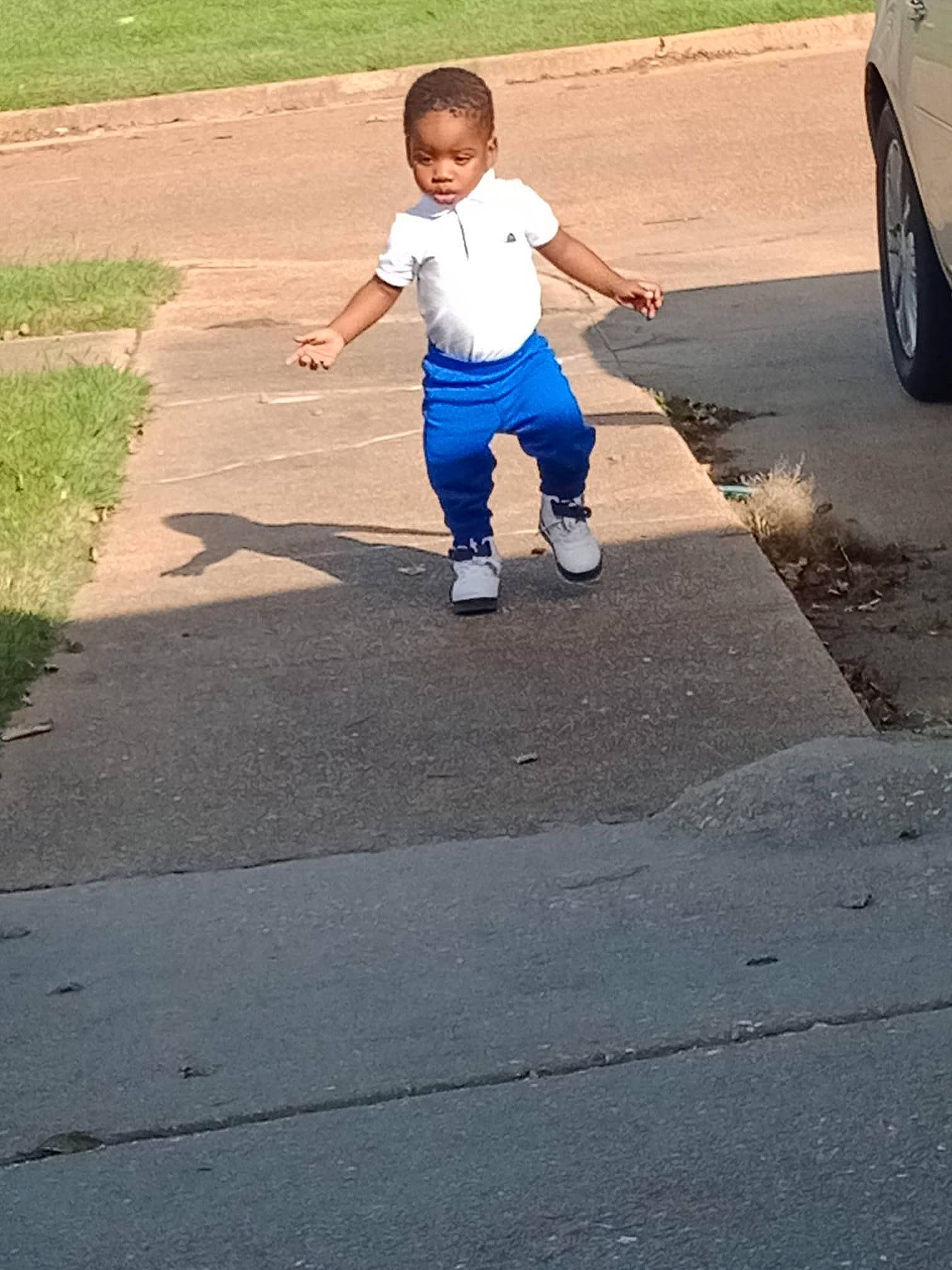 Ezekiel is registered to the contest to win money with this photo: asphalt, ball, electric_blue, flooring, gesture, grass, leisure, pedestrian, person, plant, recreation, road, road_surface, sidewalk, sports_equipment, tints_and_shades, tire, toddler, tree, walking