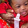 Dream Legacy is registered to the contest to win money with this photo: baby, infant, child, red_clothing, hand, face, tongue_out, festive, candy_cane_pattern, holiday, close_up, skin, person, cute, smiling, holding, warm, indoors, expression, portrait