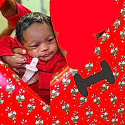 Dream Legacy is registered to the contest to win money with this photo: baby, infant, red_clothing, face, hand, floral_pattern, wrapping_paper, heart_shape, love, gift_wrap, cute, portrait, person, celebration, holiday, holding, closeup, indoors, expression, smile