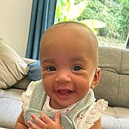 Eva participe au concours pour gagner de l'argent avec cette photo : baby, smiling, face, child, indoor, couch, pillow, clothing, person, happy, cute, infant, furniture, window, curtain, greenery, hand, eyes, portrait, ruffled_sleeves